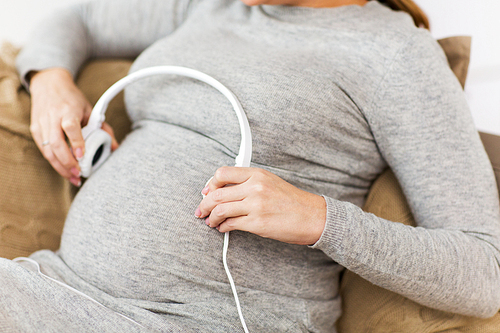 pregnancy, technology and people concept - close up of pregnant woman with headphones on her belly at home