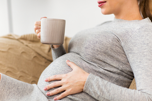 pregnancy, people and expectation concept - close up of happy pregnant woman with cup drinking tea at home