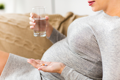 pregnancy, healthcare, people and medicine concept - close up of pregnant woman with pills and water at home