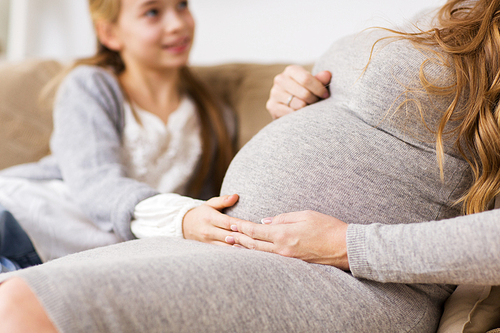 pregnancy, people and family concept - close up of pregnant woman with girl sitting on sofa and talking at home