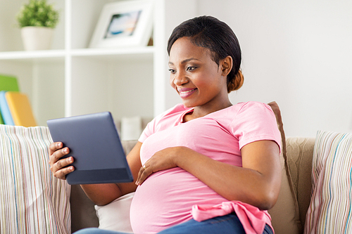 pregnancy, technology and people concept - happy pregnant african american woman with tablet pc computer at home