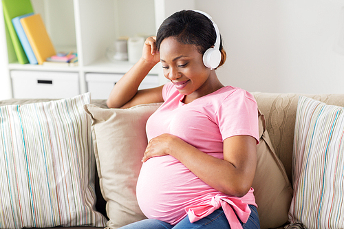 pregnancy, technology and people concept - happy pregnant african american woman with headphones listening to music at home