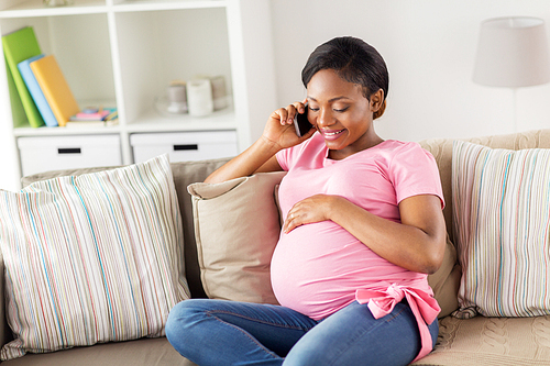 pregnancy, technology and people concept - happy pregnant african american woman calling on smartphone at home