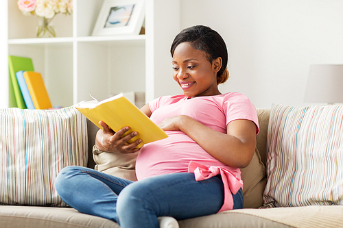 pregnancy and leisure concept - smiling pregnant african american woman reading book at home