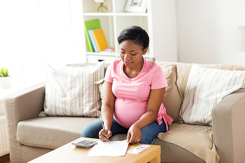 finances, pregnancy and people concept - pregnant african american woman with calculator and money filling papers at home