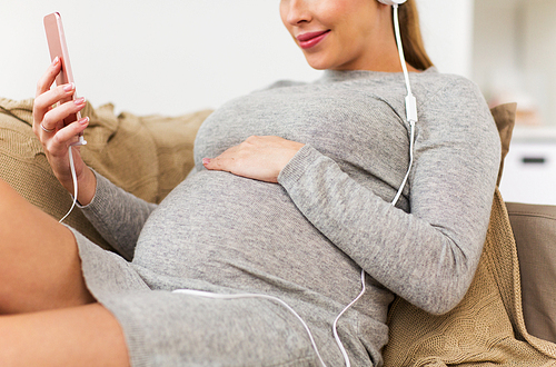 pregnancy, technology and people concept - happy pregnant woman with smartphone and headphones listening to music at home