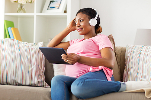 pregnancy, technology and people concept - happy pregnant african american woman with headphones and tablet pc computer at home