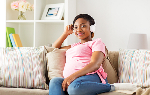 pregnancy, technology and people concept - happy pregnant african american woman with headphones listening to music at home