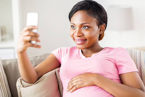 pregnancy, people and technology concept - happy pregnant african american woman with smartphone taking selfie at home
