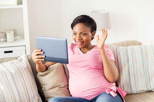 pregnancy, technology and people concept - happy pregnant african american woman with tablet pc computer having video call and waving hand at home