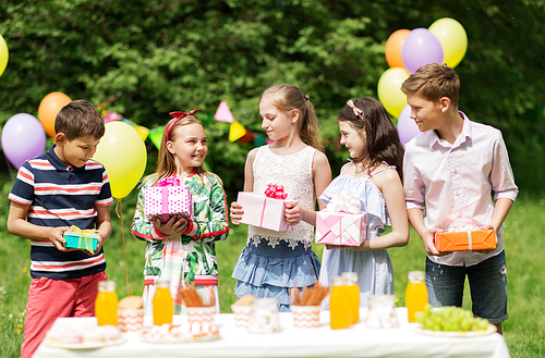 holidays, childhood and celebration concept - happy kids with gifts on birthday party at summer garden