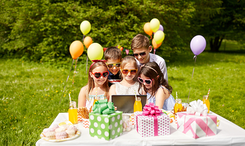 holidays, childhood and technology concept - happy kids in sunglasses with tablet pc on birthday party at summer garden