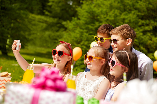 holidays, childhood and technology concept - happy kids in sunglasses taking selfie on birthday party at summer garden