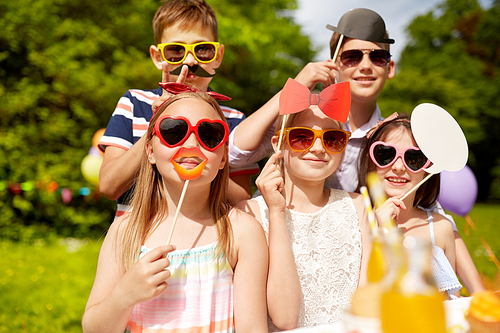 holidays, childhood and celebration concept - happy kids with party props on birthday in summer garden