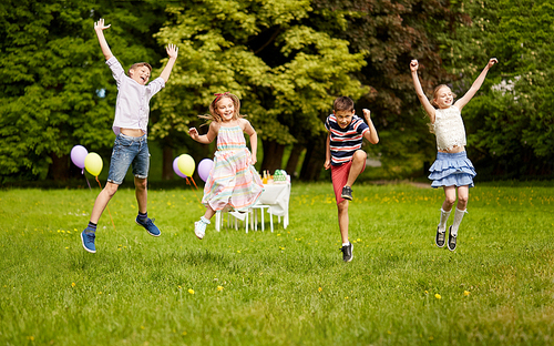 holidays, childhood and celebration concept - happy kids having fun and jumping on birthday party at summer park