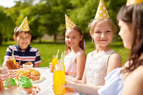 holidays, childhood and celebration concept - happy kids sitting at table on birthday party at summer garden