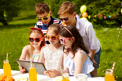 holidays, childhood and technology concept - happy kids in sunglasses with tablet pc on birthday party at summer garden