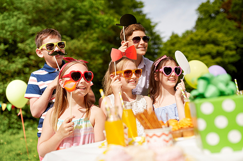 holidays, childhood and celebration concept - happy kids with party props on birthday in summer garden
