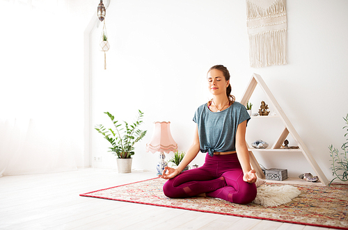 mindfulness, spirituality and healthy lifestyle concept - woman meditating in lotus pose at yoga studio