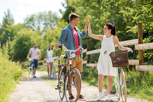 people, leisure and lifestyle concept - happy young couple riding fixed gear bicycles in summer making high five