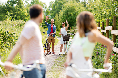 people, leisure and lifestyle concept - happy young friends with fixed gear bicycles in summer waving hands