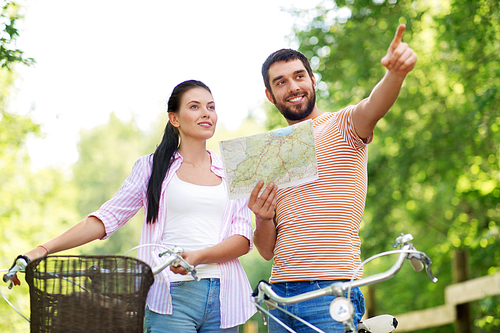 travel, trip, leisure and lifestyle concept - happy young couple with map and bicycles looking for location at country in summer