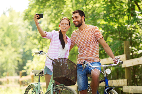 people, technology and lifestyle concept - happy couple with bicycles taking selfie by smartphone at summer park