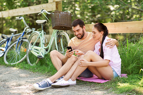 people, technology and lifestyle concept - happy couple with smartphone and bicycles at summer park