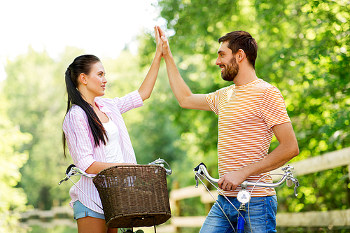 people, leisure and lifestyle concept - happy young couple with bicycles at country making high five at summer park
