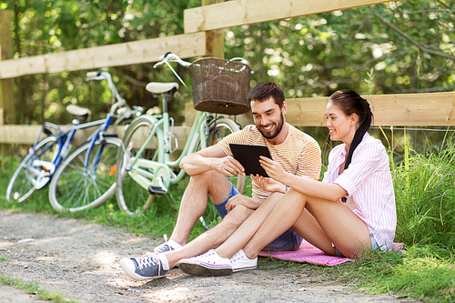 people, technology and lifestyle concept - happy couple with tablet pc computer and bicycles at summer park