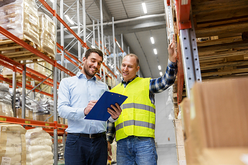 wholesale, logistic business and people concept - manual worker and businessman with clipboards at warehouse