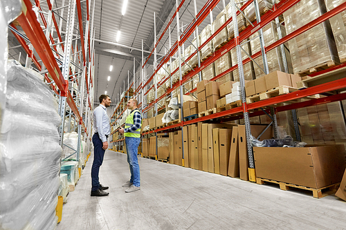 logistic business, shipment and people concept - male worker and businessman with clipboards at warehouse