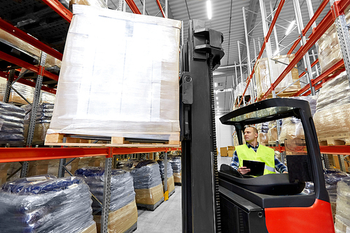 logistic business, shipment and loading concept - loader with clipboard and cargo on forklift at warehouse