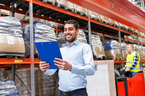 logistic business, shipment and people concept concept - happy businessman with clipboard at warehouse