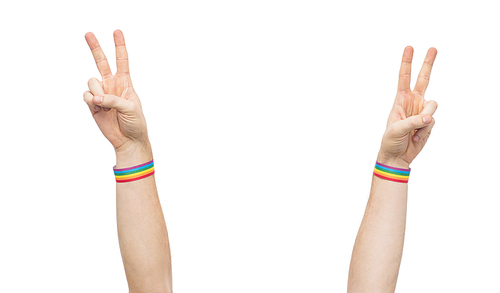 lgbt, same-sex relationships and homosexual concept - close up of male hands wearing gay pride awareness wristbands showing peace sign