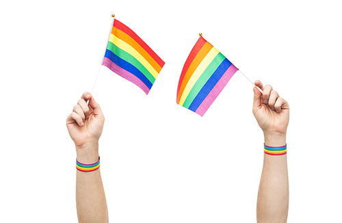 lgbt, same-sex relationships and homosexual concept - close up of male hand wearing gay pride awareness wristbands holding rainbow flags