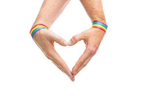 lgbt, same-sex love and homosexual relationships concept - close up of male couple hands with gay pride rainbow awareness wristbands showing heart gesture