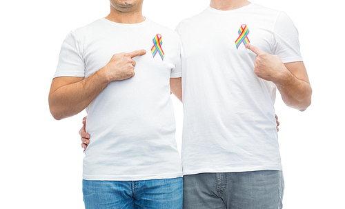 lgbt, same-sex relationships and homosexual concept - close up of happy male couple pointing at gay pride rainbow awareness ribbons on chest