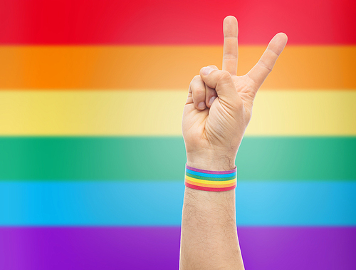 lgbt, same-sex relationships and homosexual concept - close up of male hand wearing gay pride awareness wristband showing peace sign