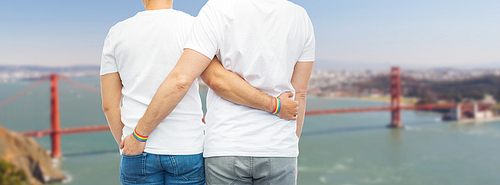 lgbt, same-sex relationships and homosexual concept - close up of hugging male couple wearing rainbow gay pride awareness wristbands over golden gate bridge in san francisco bay background