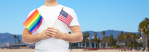 lgbt, same-sex relationships and homosexual concept - close up of man holding gay pride rainbow and american flag over venice beach background in california