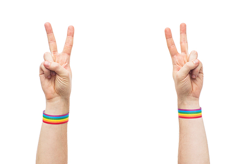 lgbt, same-sex relationships and homosexual concept - close up of male hands wearing gay pride awareness wristbands showing peace sign