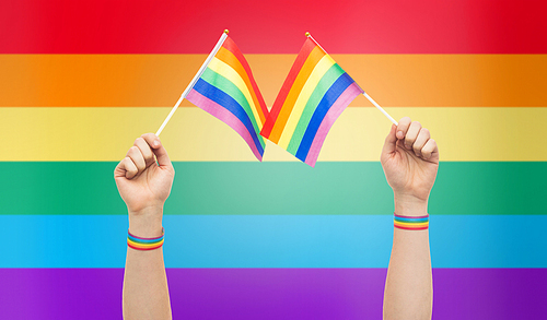 lgbt, same-sex relationships and homosexual concept - close up of male hand wearing gay pride awareness wristbands holding rainbow flags