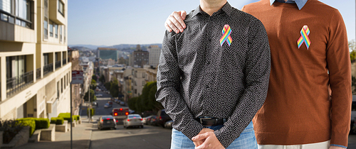 lgbt, same-sex relationships and homosexual concept - close up of male couple with gay pride rainbow awareness ribbons over san francisco city background