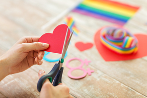 homosexual and lgbt concept - female hands with scissors cutting out red paper heart decoration for gay party