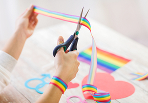 homosexual and lgbt concept - female hands with scissors cutting gay pride awareness ribbon