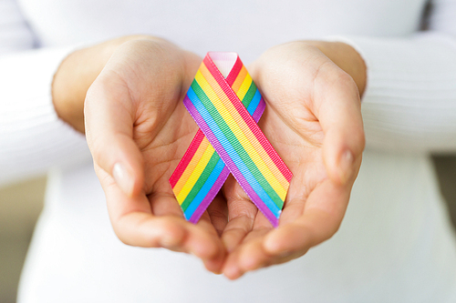 homosexual and lgbt concept - close up of female hands holding gay pride awareness ribbon