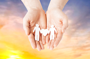 lgbt and gay concept - hands holding paper male couple pictogram with heart over evening sky background