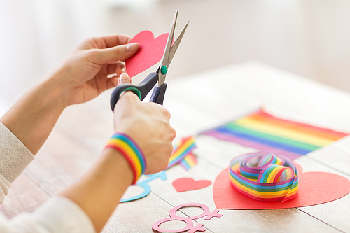 homosexual and lgbt concept - female hands with scissors cutting out red paper heart decoration for gay party