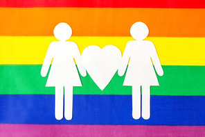 gay pride, homosexual and lgbt concept - female couple white paper pictogram on rainbow flag background